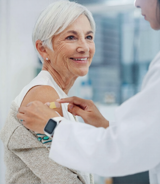 Smiling older woman receiving a bandage on her arm from a healthcare professional, emphasizing patient care in a clinical setting related to wellness and anti-aging treatments.